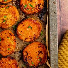 baked sweet potatoes in a baking pan with herbs on top and seasoning next to them