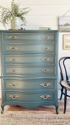 a blue dresser with gold handles and knobs on the drawers, next to a chair