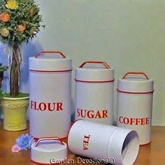 four white canisters sitting on top of a wooden table next to a potted plant