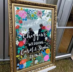 a wedding sign in front of a window with flowers on it and two people holding hands