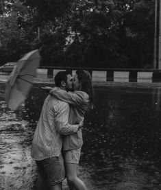 a man and woman kissing in the rain with an umbrella over their heads as they hug