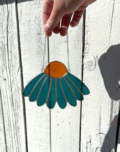 a hand holding a blue and orange flower shaped glass ornament on a chain