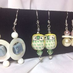 four pairs of owl earrings with pearls and glass beads on black velvet holder, sitting on white fabric