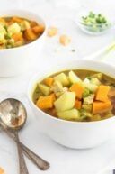 two bowls filled with soup on top of a white table next to silver spoons