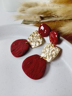 three red and gold earrings sitting on top of a white plate next to some feathers