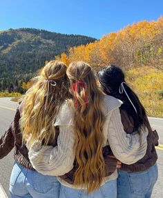 three girls are standing on the side of the road with their arms around each other