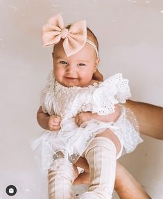 a baby girl with a big bow on her head is smiling at the camera while being held by someone