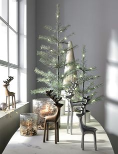 christmas trees and deers are sitting on a table in front of a large window