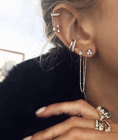 a close up of a person wearing ear rings and chain bracelets on their fingers