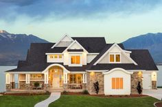 a large house with lots of windows in front of the water and mountains behind it