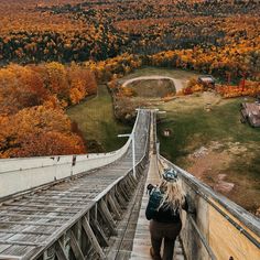 a woman walking up the side of a wooden walkway over a forest filled with trees