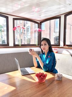 a woman sitting at a wooden table with a laptop and fruit in front of her