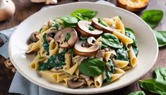 a white bowl filled with pasta and mushrooms on top of a wooden table next to green leaves