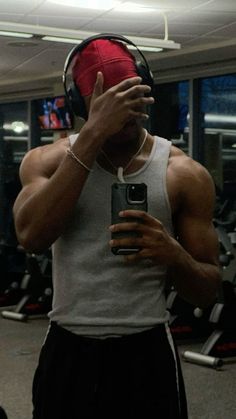 a man with headphones on taking a selfie in the gym while holding a cell phone