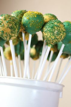 green and yellow cake pops with sprinkles in a white cup on a table