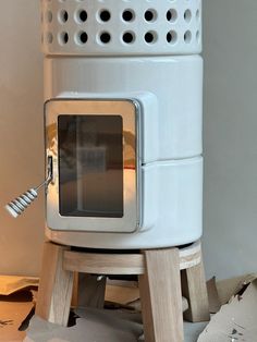 a white stove sitting on top of a wooden stand next to a wall with holes in it