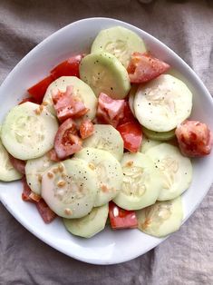 a white bowl filled with cucumbers and tomatoes on top of a table cloth