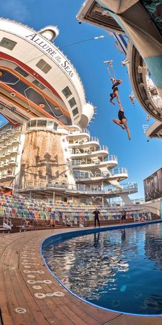 two people jumping off the side of a large cruise ship into a swimming pool in front of a multi - story building