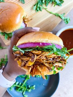 a hand holding a pulled pork sandwich over a blue plate