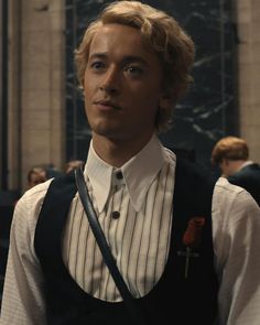 a young man with blonde hair wearing a black vest and suspenders