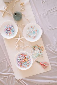 three white bowls filled with sprinkles on top of a table next to scissors