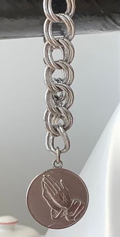 This beautiful Monet bracelet is a perfect addition to any jewelry collection. The sterling silver bracelet features a charming dangle charm with praying hands on the front and the serenity prayer on the back. The bracelet is 6 inches in length and has a double link chain type.  The bracelet is perfect for any occasion, whether it be a Christmas gift, anniversary gift, or birthday gift. It is also signed by the Monet brand, adding a touch of authenticity to the piece. The vintage style and relig White Gold Metal Chain Bracelet With Charms, White Gold Chain Bracelet With Charms, Symbolic Dangle Bracelets With Charms, Silver Charms Chain Bracelet For Everyday, Silver Stainless Steel Chain Bracelet With Charms, Spiritual Silver Jewelry With Dangling Charms, Everyday Spiritual Charm Bracelet, Adjustable Silver Bracelet With Round Pendant, Everyday Silver Charm Bracelet With Lobster Clasp