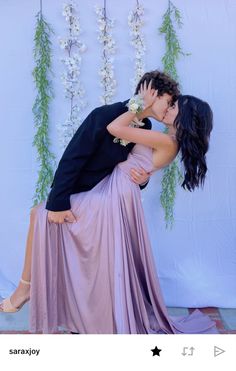 a man and woman kissing each other in front of a wall with flowers on it