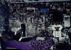 a woman sitting on top of a bed next to a wall covered in pictures and posters