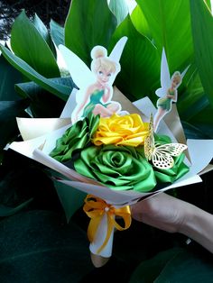 a hand holding a paper bouquet with flowers and tinkerbell figurines on it