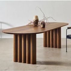 a wooden table sitting on top of a white floor next to a chair and vase