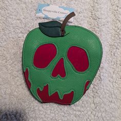 an apple with a green and red skull painted on it's side sitting on a white surface