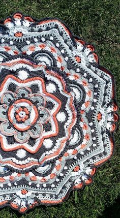 a crocheted doily on the ground with grass in the foreground and an orange and white flower