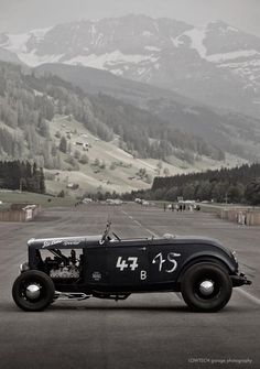 an old car is parked on the road in front of some mountains and snow covered hills