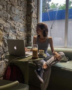 a woman sitting at a table with a laptop computer in front of her, looking out the window