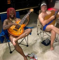 two men sitting in chairs with guitars on their feet and one man holding an electric guitar