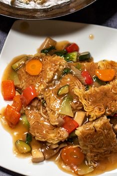 a white plate topped with meat and veggies covered in gravy next to a skillet