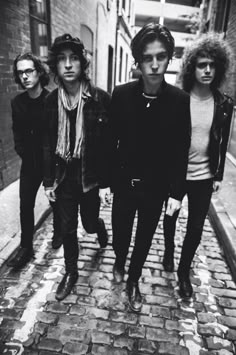 an old black and white photo of four young men walking down a brick street with one man looking at the camera