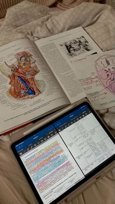 an open book sitting on top of a bed next to a laptop computer and tablet