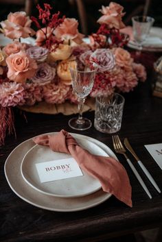 a place setting with pink flowers and napkins on the table for an elegant dinner