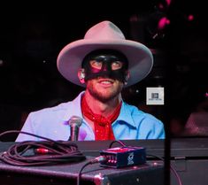 a man wearing a cowboy hat and blindfold with a microphone in front of him