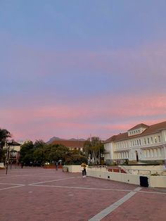 people are walking around in an empty parking lot with buildings on either side and pink skies overhead