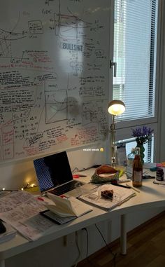 a white board with writing on it next to a lamp and desk in front of a window