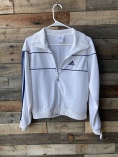 Sweet Adidas jacket! Features Include... Adidas track jacket White with navy blue stripes and embroidered logo "The Brand With the Three Stripes" Zip front Made by Adidas Tag size USA medium (please see measurements below for most accurate sizing) Condition... Excellent vintage condition - no holes, flaws or other issues. Jacket is clean and ready to wear! Measurements... Shoulder to shoulder - 15"  Sleeve length - 24" Around chest, underneath armpits - 38 1/2"  Waist - 36 1/2" with elastic for Y2k Adidas, Adidas Track Jacket, Adidas Track, Adidas White, Stretch Top, Vintage Adidas, White Adidas, Navy Stripes, Track Jacket