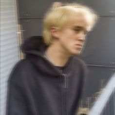 a young man with blonde hair wearing a black hoodie and looking off to the side