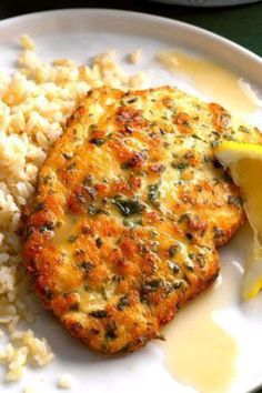 a white plate topped with meat and rice covered in gravy next to a lemon wedge