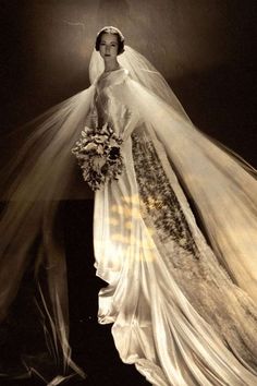 an old photo of a woman in a wedding dress with veil over her head and flowers on the skirt