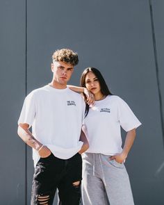 two people standing next to each other wearing white t - shirts and black ripped jeans