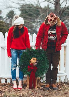 a man and woman standing next to a dog with a wreath on it's neck