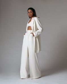 a woman standing in front of a gray background wearing a white suit and matching heels