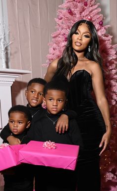 a woman posing with her three children in front of a christmas tree and pink presents